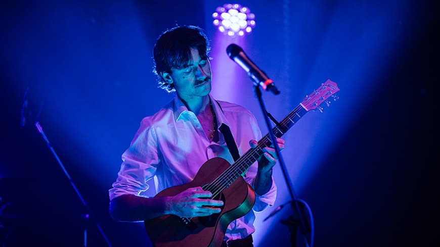 Charlie Youngson performing on stage under blue lighting while playing an acoustic guitar.